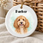 Personalized ceramic pet ornament with a watercolor dog portrait, Parker name and mint background beside wicker and linen.